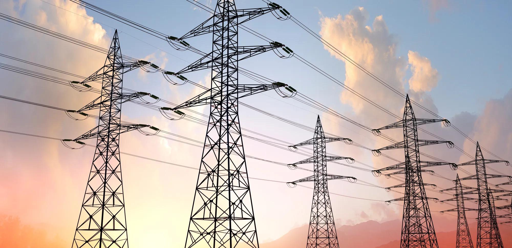 Eine Panoramaaufnahme einer Stromtrasse aus zwei parallel verlaufenden Strommastreihen. Im Hintergrund der Himmel eingefärbt im Sonnenuntergang.