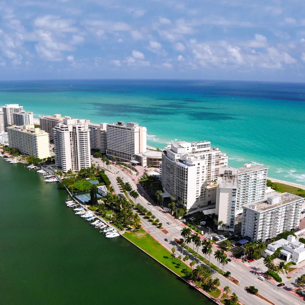 Küstenstadt mit weißen Hochhäusern, grünem Wasser und blauem Himmel, Strand im Hintergrund.
