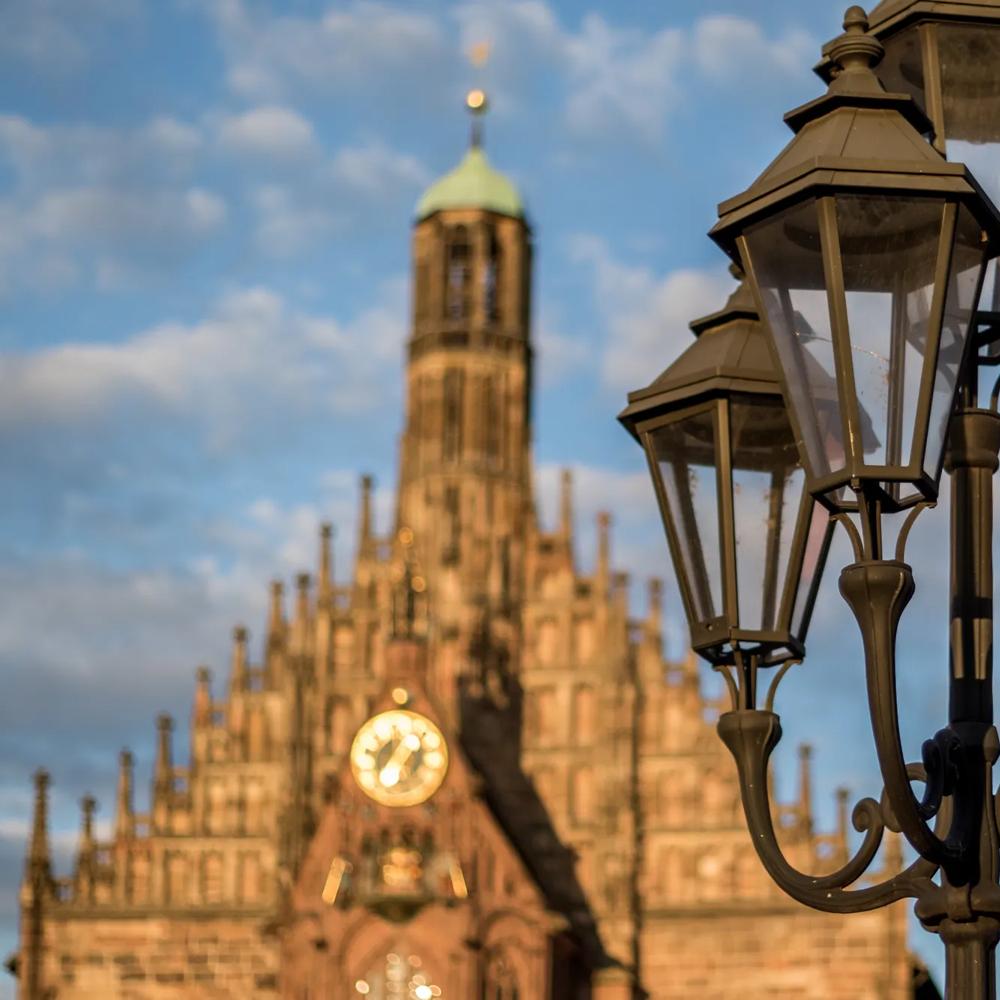 Eine Laterne vor einer gotischen Kirche mit Uhr unter blauem Himmel.