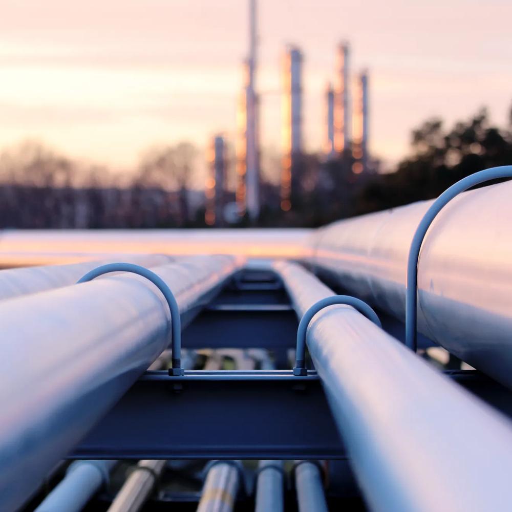 Industriepipelines bei Sonnenuntergang, im Hintergrund verschwommene Schornsteine.