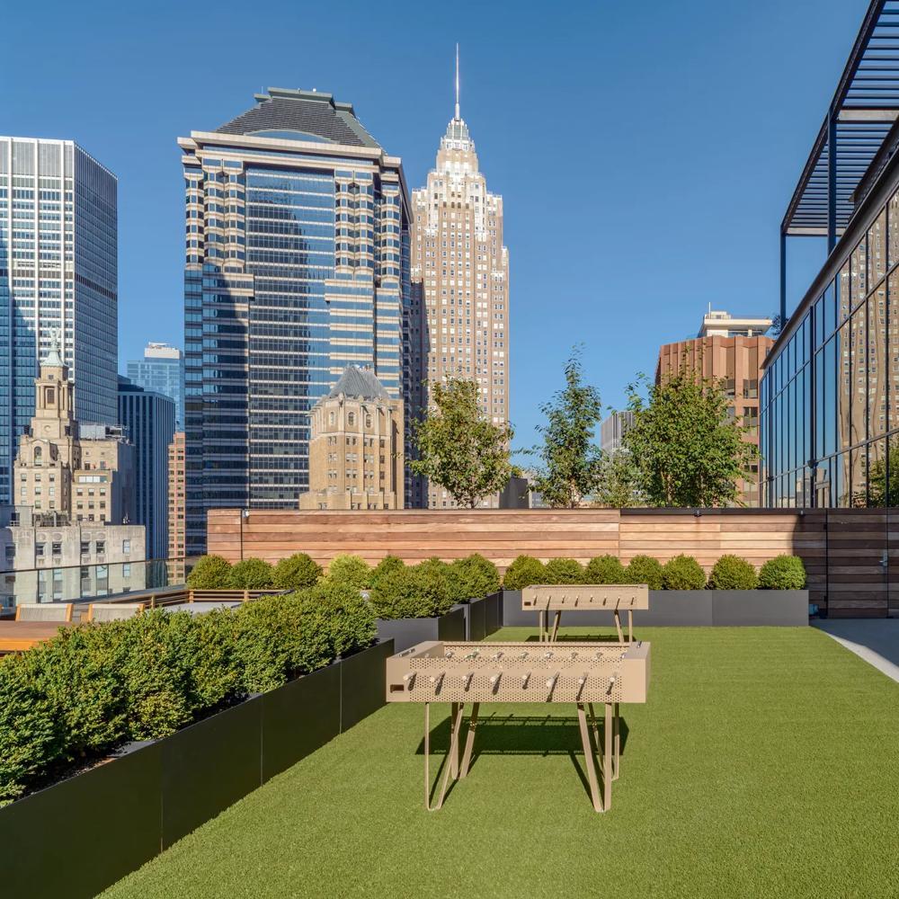Roof terrace with artificial turf, table football and high-rise buildings in the background with a clear sky.