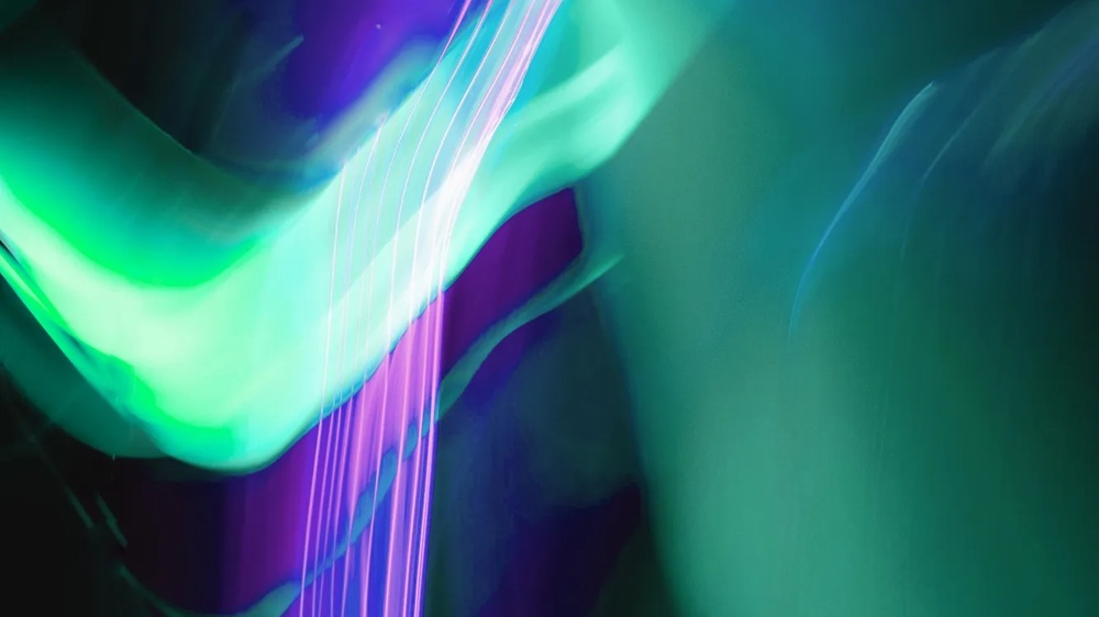 Dynamische, abstrakte Lichtlinien in Grün-, Blau- und Violetttönen mit fließender Bewegung auf dunklem Hintergrund