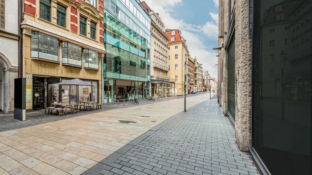 Eine leere, gepflasterte Einkaufsstraße mit historischen und modernen Gebäuden unter blauem Himmel.