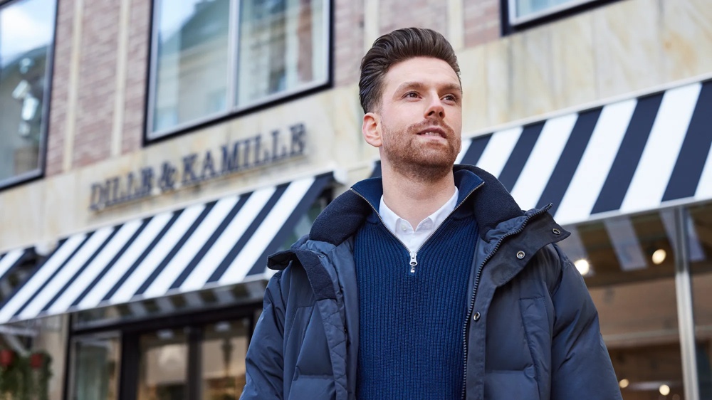 Ein Mann in blauer Jacke steht vor einem Geschäft mit schwarz-weiß gestreifter Markise.