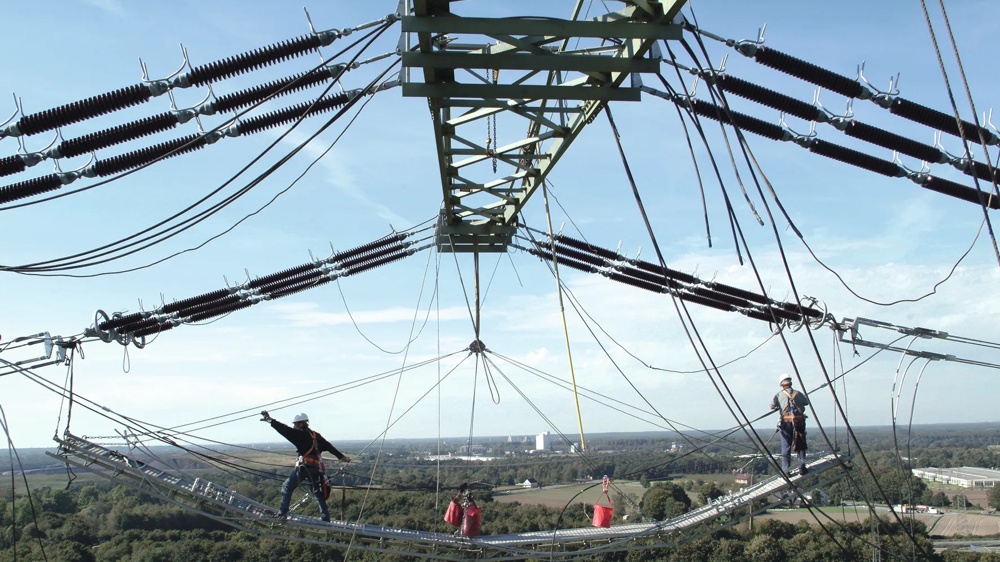 Arbeiter auf Strommast, gesichert, mit Landschaft im Hintergrund.
