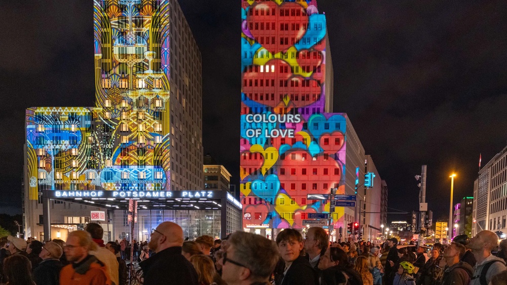 Mehrgeschossiges Gebäudeensemble bei Nacht mit großflächigen farbigen Lichtprojektionen auf den Fassaden.