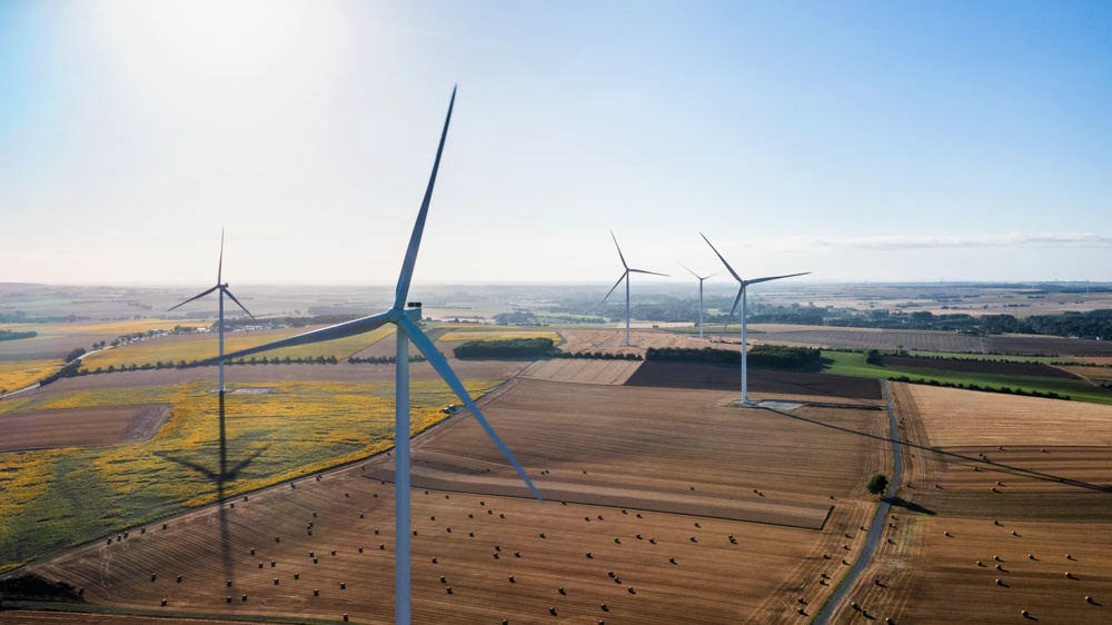 Windräder auf einem Feld bei Sonnenuntergang, mit weitläufigem Himmel und sanften Wolken.