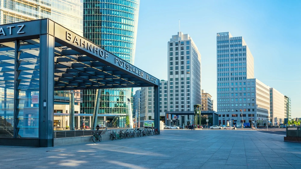 Eingang zum Bahnhof Potsdamer Platz, umgeben von modernen Hochhäusern unter klarem blauem Himmel.
