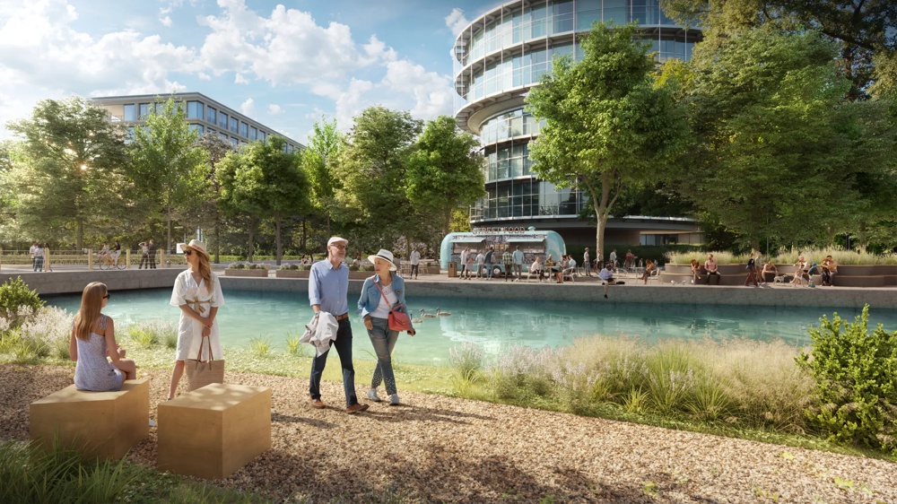 People are walking around a pond with ducks, trees and modern buildings in the background.