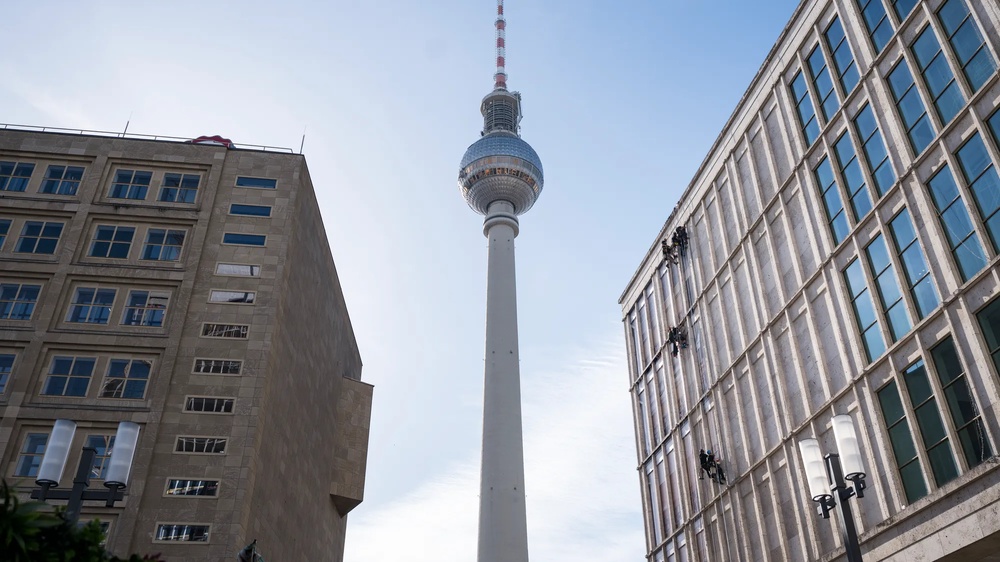 Am Berliner Alexanderplatz wird die Fassade der Galeria-Filiale gezeigt, wie sie von Fassadenkletterern mit bedruckten Klebebahnen versehen wird. die Bahnen visualisieren die mögliche neue Innengestaltung des Gebäudes als offene Bibliothek.