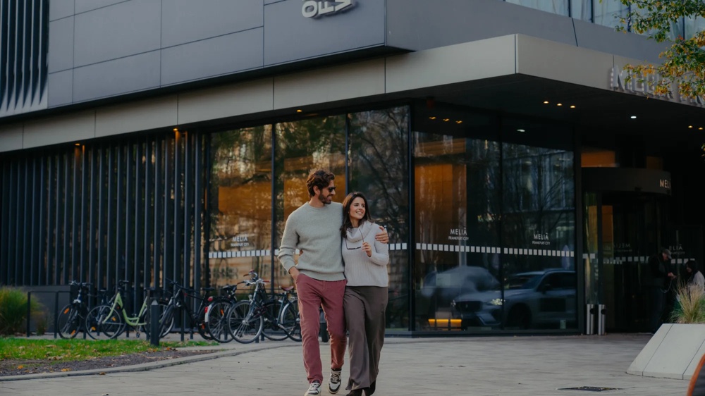Zwei Personen gehen im Außenbereich vor einem Gebäude.