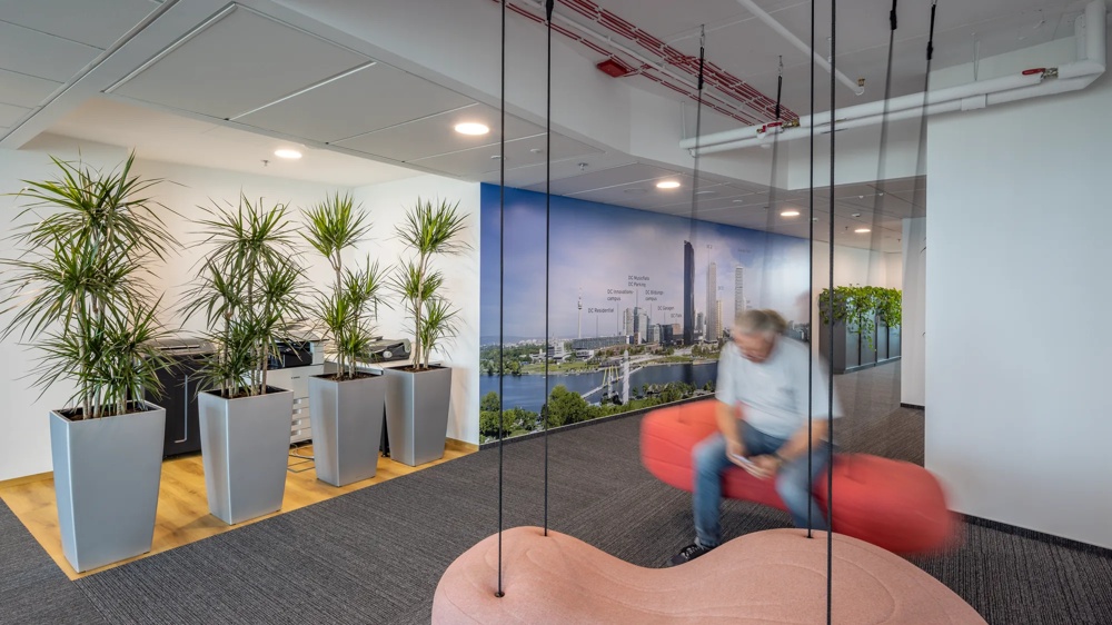 Ein Büro mit modernen Pflanzen, einer Wand mit Stadtbild und einer Person auf einer roten Schaukel.
