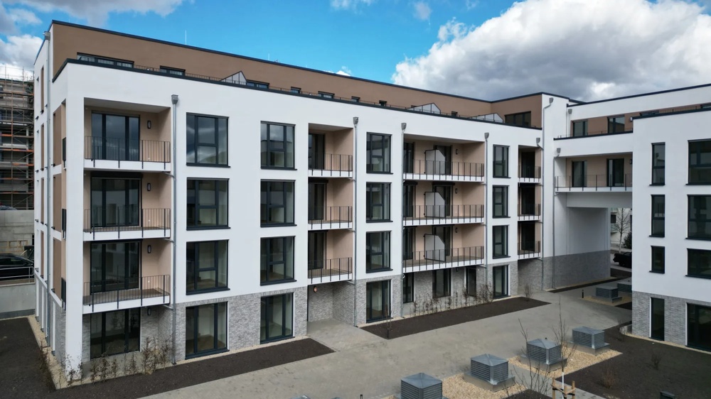Moderne, mehrstöckige Wohnanlage mit weißen Fassaden, großen Fenstern und Balkonen unter blauem Himmel.