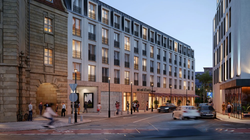Visualisierung der Außenfassade des Krystallpalast-Areals in Leipzig bei Abenddämmerung – historische Sandsteinfassade mit modernem Neubauflügel und „me and all hotels"-Schriftzug im Erdgeschoss – ein hausInvest-Objekt.