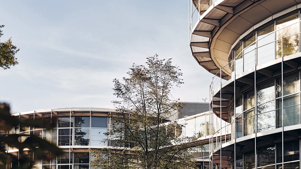 Moderne Glasfassade mit Bäumen und Gehweg im Vordergrund.