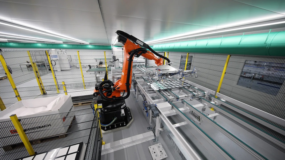 Ein orangefarbener Industrieroboter bewegt Glasplatten in einer modernen Fabrikhalle.