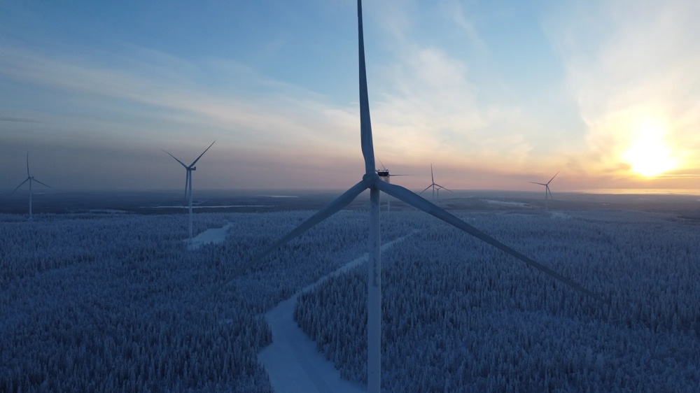 Windmills over snow-covered forest at sunset, blue sky.