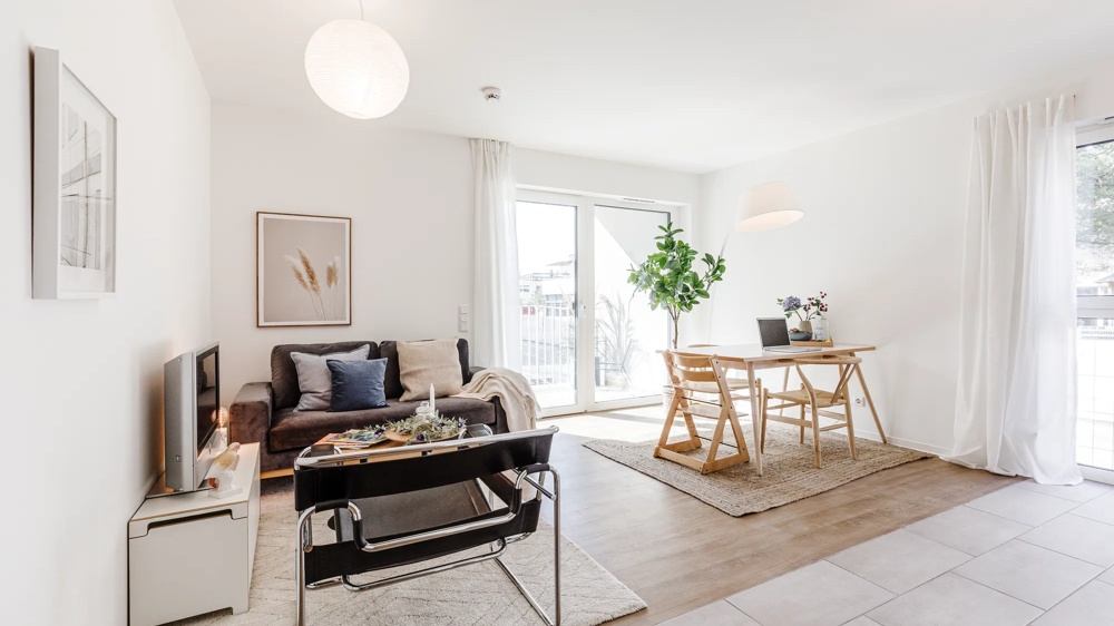 Bright living room with sofa, table, chair, large windows and plants. Modern, minimalist interior.