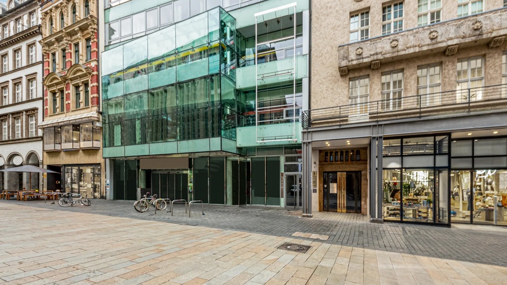 Moderne Glasfassade zwischen historischen Gebäuden, leere Pflasterstraße, Fahrräder am Ständer.