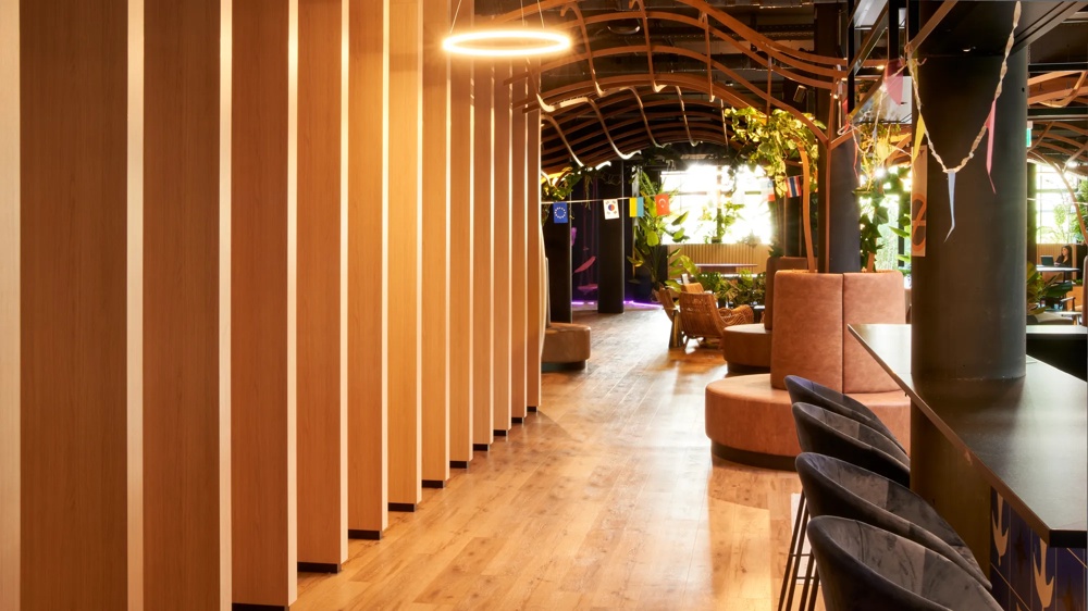 Modern space with wooden walls, bar stools and plants; warm lighting and cosy seating areas.