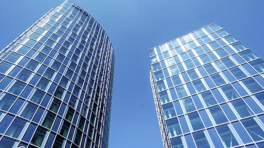 Two modern glass buildings stand out in the blue sky.