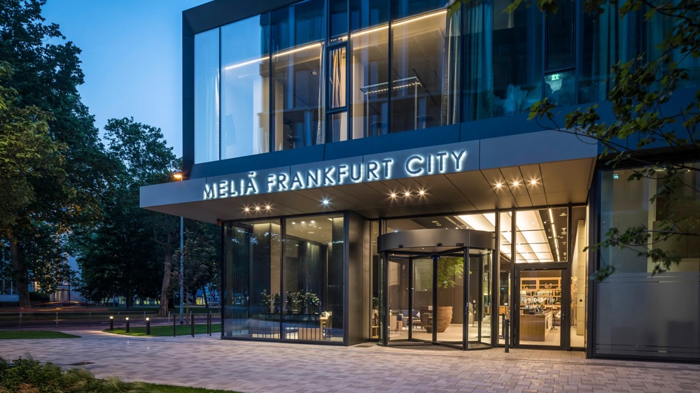 Eingang des Melia Frankfurt City Hotels bei Dämmerung, mit Glasfront und beleuchtetem Schriftzug.