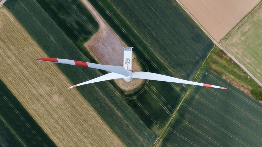 Zwei Windräder stehen auf einem weiten Feld unter bewölktem Himmel bei Sonnenuntergang.