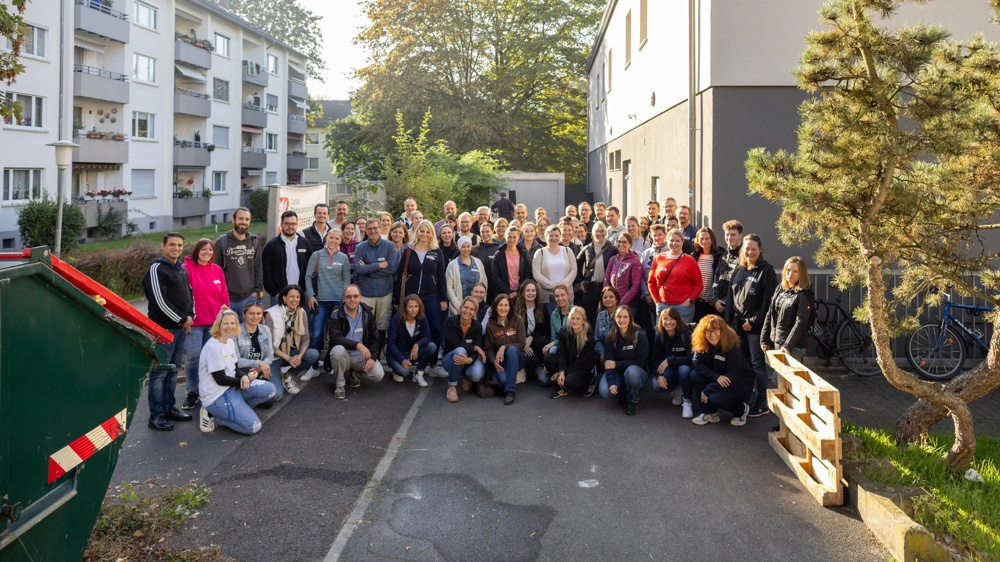 A large group of people standing outside in front of a building in sunny weather.