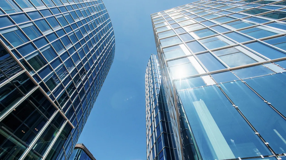 Hohe Glasgebäude ragen in den blauen Himmel, Sonnenlicht spiegelt sich in den Fenstern.