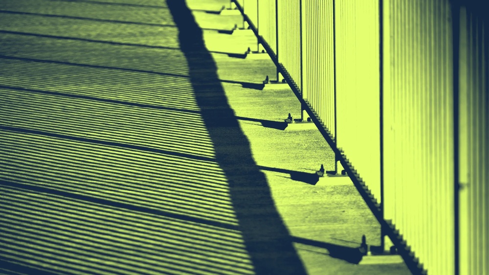 Schatten von Geländerstäben werfen parallele Linien auf einen Gehweg in gelbem Licht.