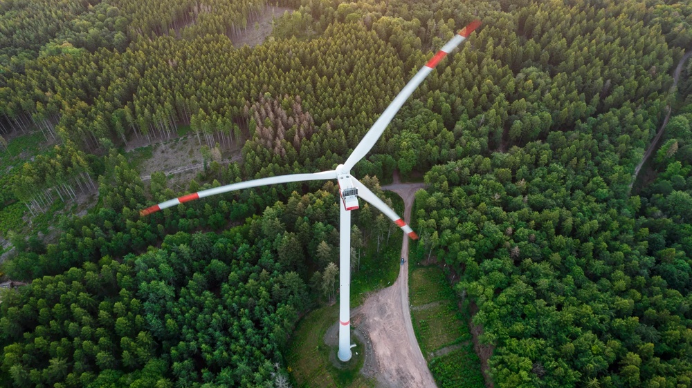 Eine Windkraftanlage steht inmitten eines dichten Waldes aus der Vogelperspektive.