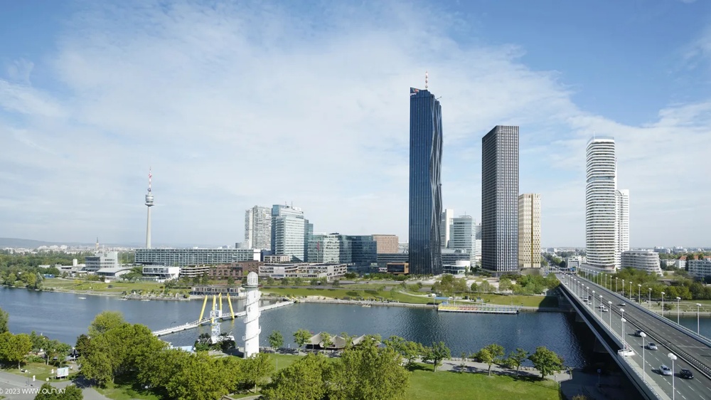 Moderne Skyline mit hohen, schlanken Türmen, Fluss im Vordergrund und Brücke, blauer Himmel mit leichten Wolken.