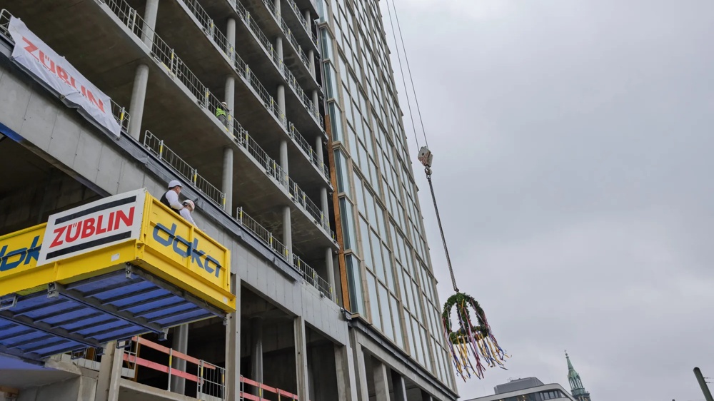 Hochhausrohbau mit Gerüsten. Der Richtspruch wird von einem gelben Grüstanbau gerufen.