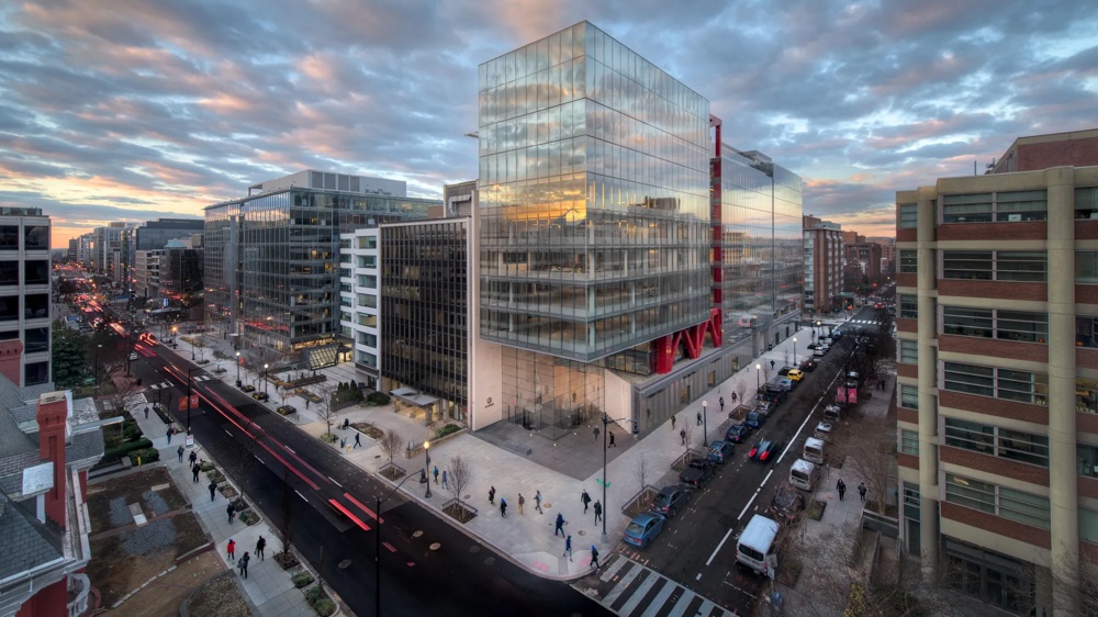 Moderne Stadtansicht bei Sonnenuntergang mit Glasgebäuden, belebter Straße und Menschen auf den Gehwegen.