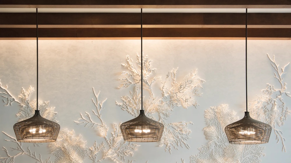 Drei hängende Lampen vor einer blauen Wand mit weißen, korallenartigen Reliefs.