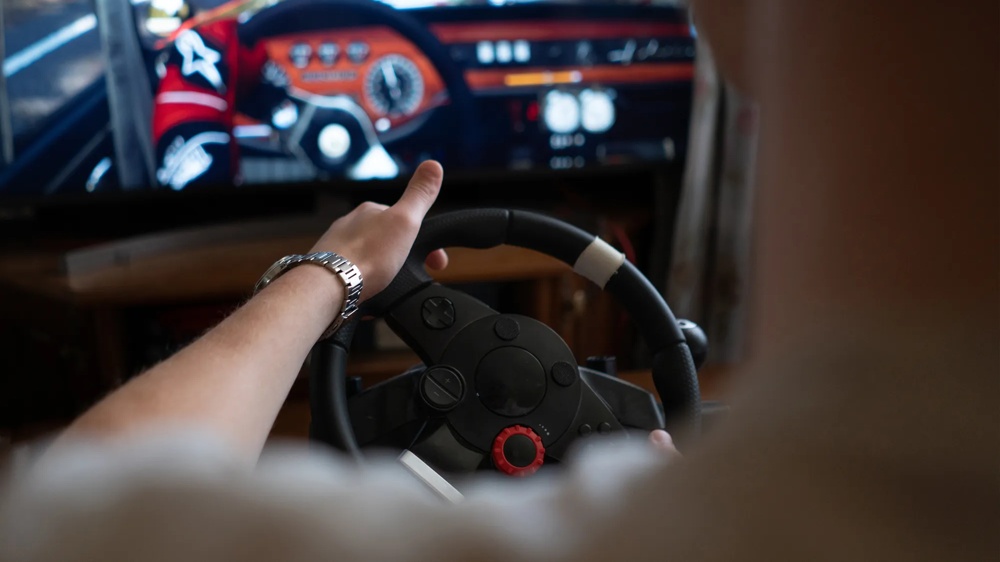 Person spielt in einem Fahrsimulator ein Autorennspiel mit Lenkrad vor einem Bildschirm.