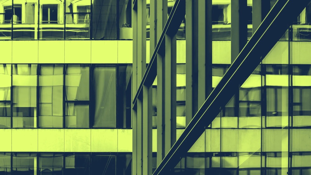 Fassadenansicht eines modernen Gebäudes mit Glas und Stahlträgern in grünlichem Licht.