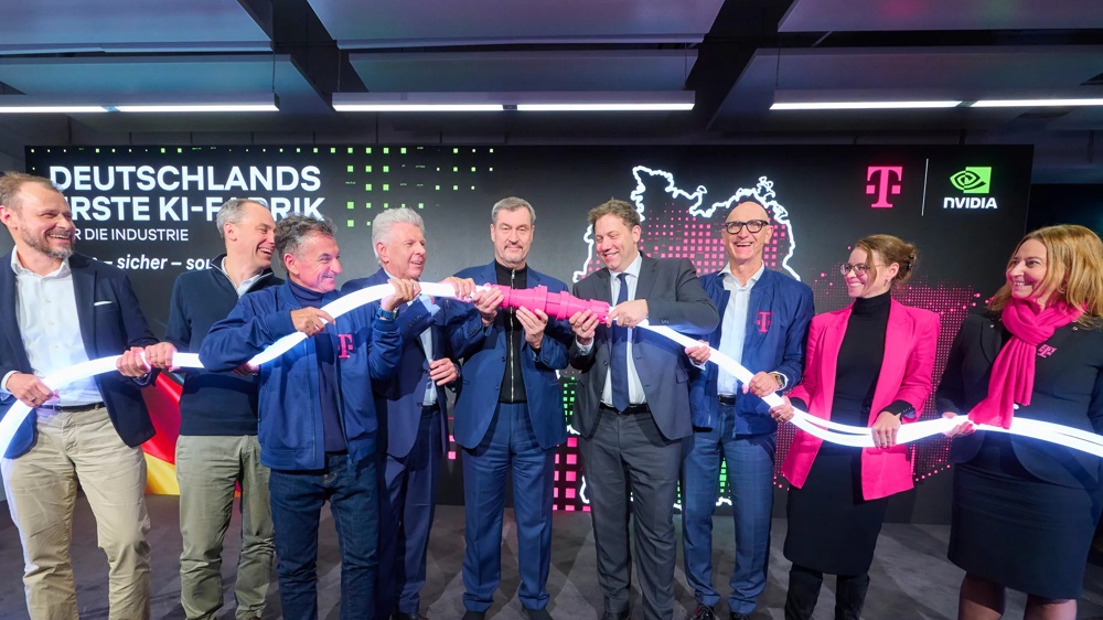 Ceremonial opening of "Germany's first AI factory." Around ten people on stage symbolically connect a cable with a magenta plug. Telekom and NVIDIA logos in the background.