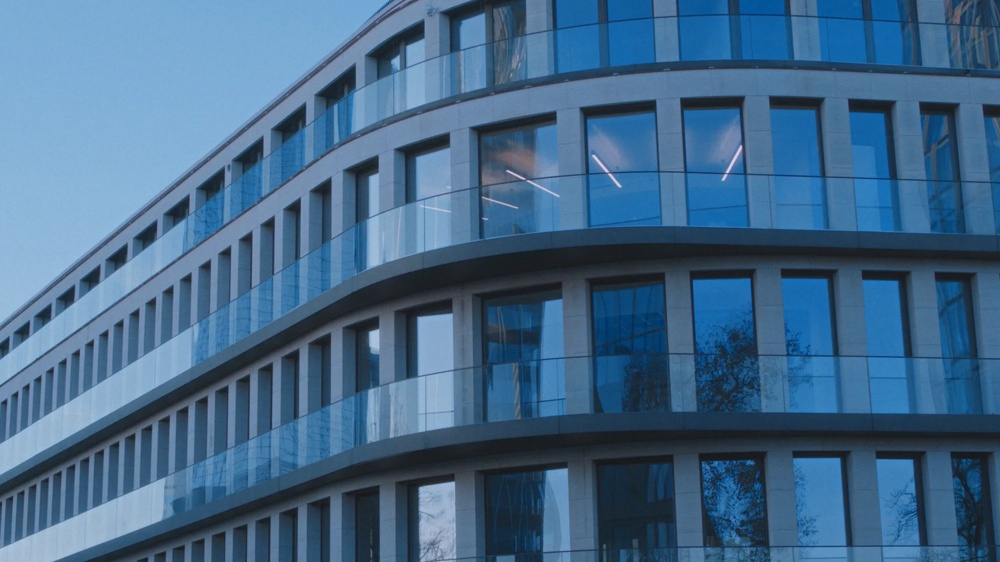 Moderne Glasfassade eines Bürogebäudes mit abgerundeten Ecken und reflektierendem Himmel.