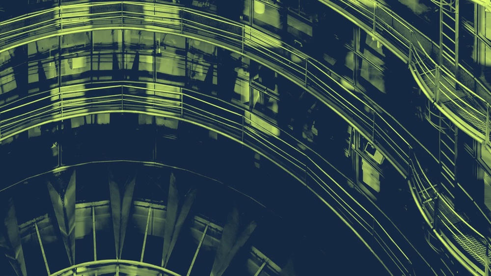 Ein spiralförmiger, moderner Glas- und Metallgang in grünlichem Licht.