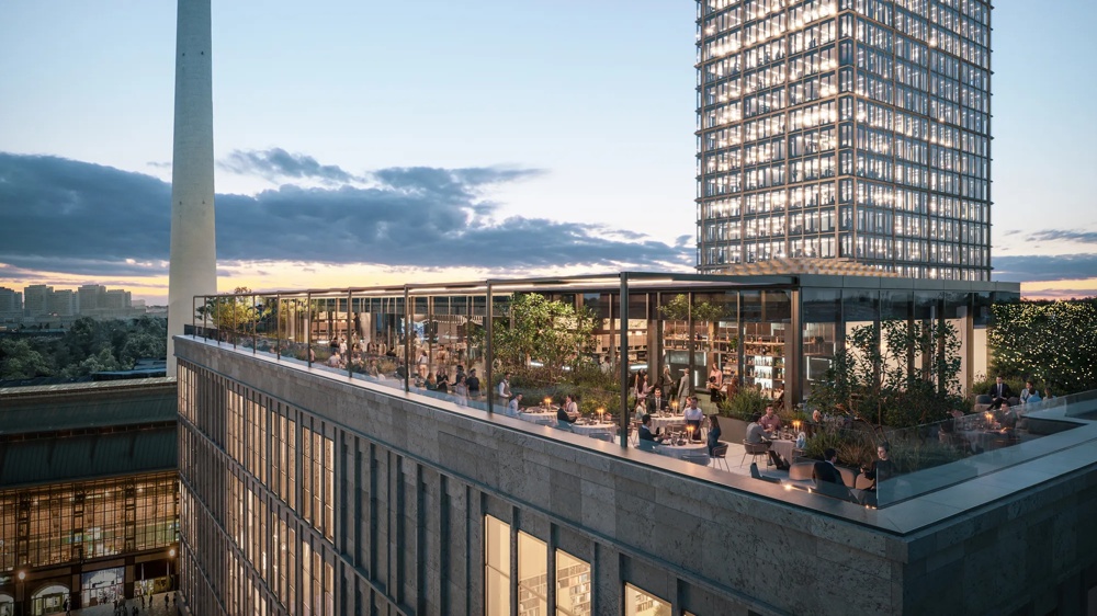 Ein Fernsehturm neben einem beleuchteten Hochhaus bei Sonnenuntergang, mit Terrasse im Vordergrund.