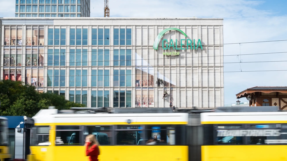 Am Berliner Alexanderplatz wird die Fassade der Galeria-Filiale gezeigt, wie sie von Fassadenkletterern mit bedruckten Klebebahnen versehen wird. die Bahnen visualisieren die mögliche neue Innengestaltung des Gebäudes als offene Bibliothek.
