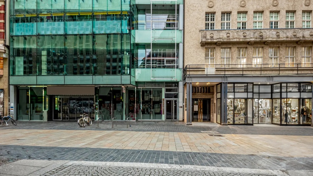 Moderne Glasfassade neben historischer Fassade, Fahrräder davor auf gepflastertem Gehweg.