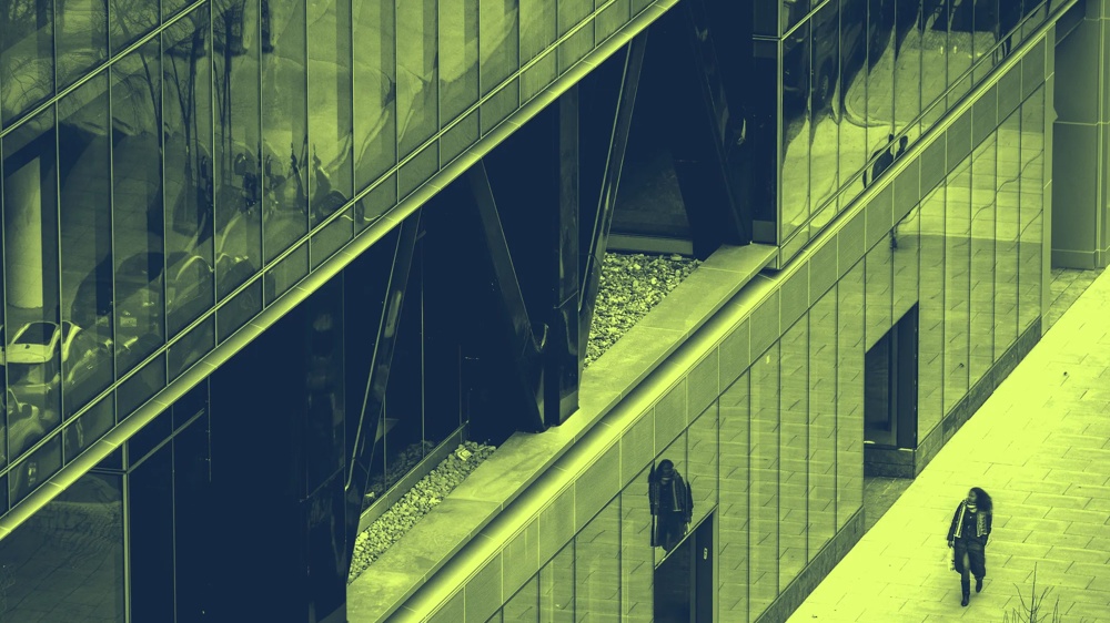 Eine Person geht an einem modernen Gebäude mit Glasfassade vorbei.