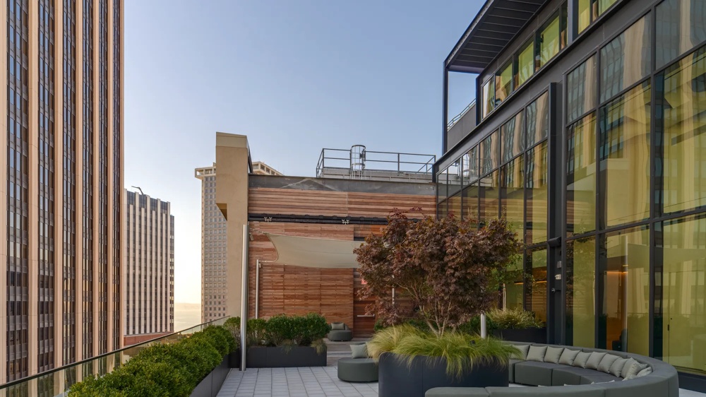 Moderne Dachterrasse mit runden Sitzgelegenheiten, Pflanzen und Glasgeländer, umgeben von hohen Gebäuden.