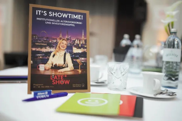 Programmheft des Institutionals-Gipfels Wien 2026 auf einem gedeckten Tisch – mit dem Titel „It's Showtime! Institutioneller Altersvorsorge- und Investorengipfel" im Late-Show-Design.