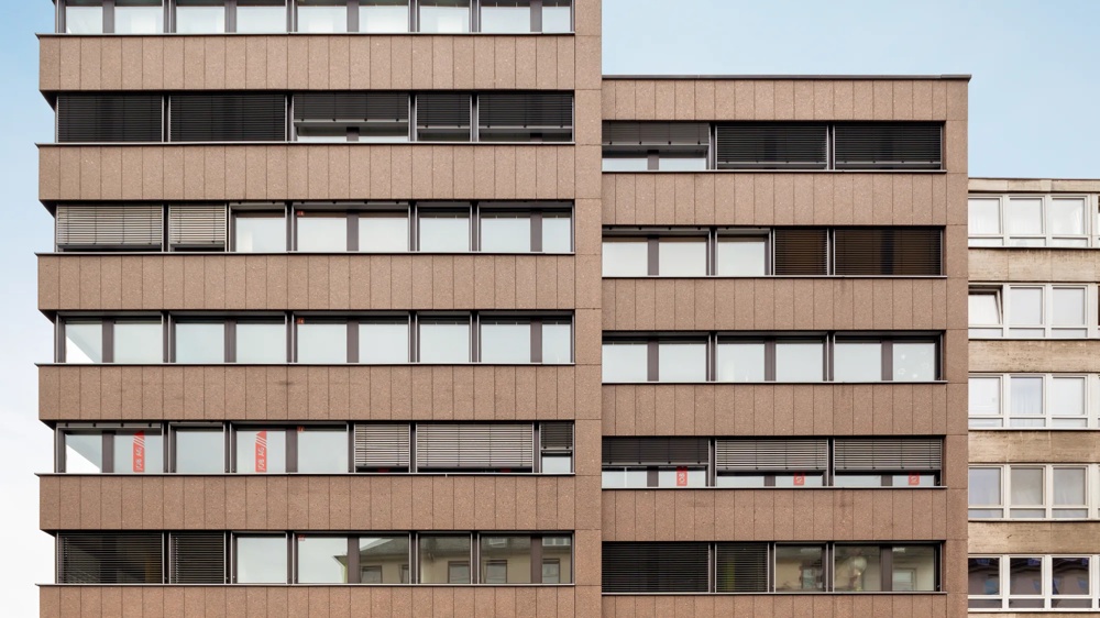 Brown, modern building with several floors and windows, blue sky in the background.