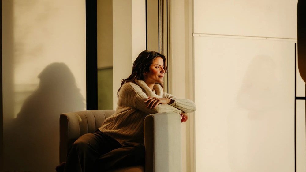 Person sitzt am Fenster einer modernen Wohnung im warmen Licht.