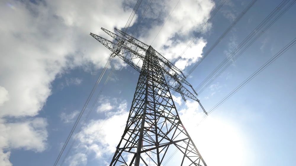 Ein Strommast ragt in den blauen Himmel, umgeben von weißen Wolken.