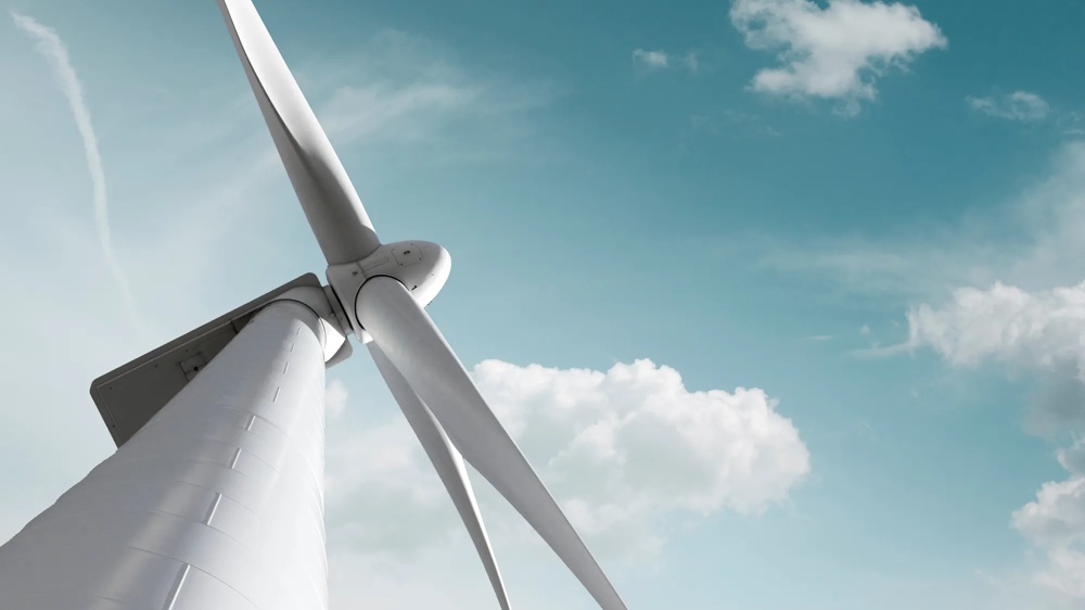 Nahaufnahme einer Windkraftanlage vor blauem Himmel mit weißen Wolken, Symbol für erneuerbare Energie